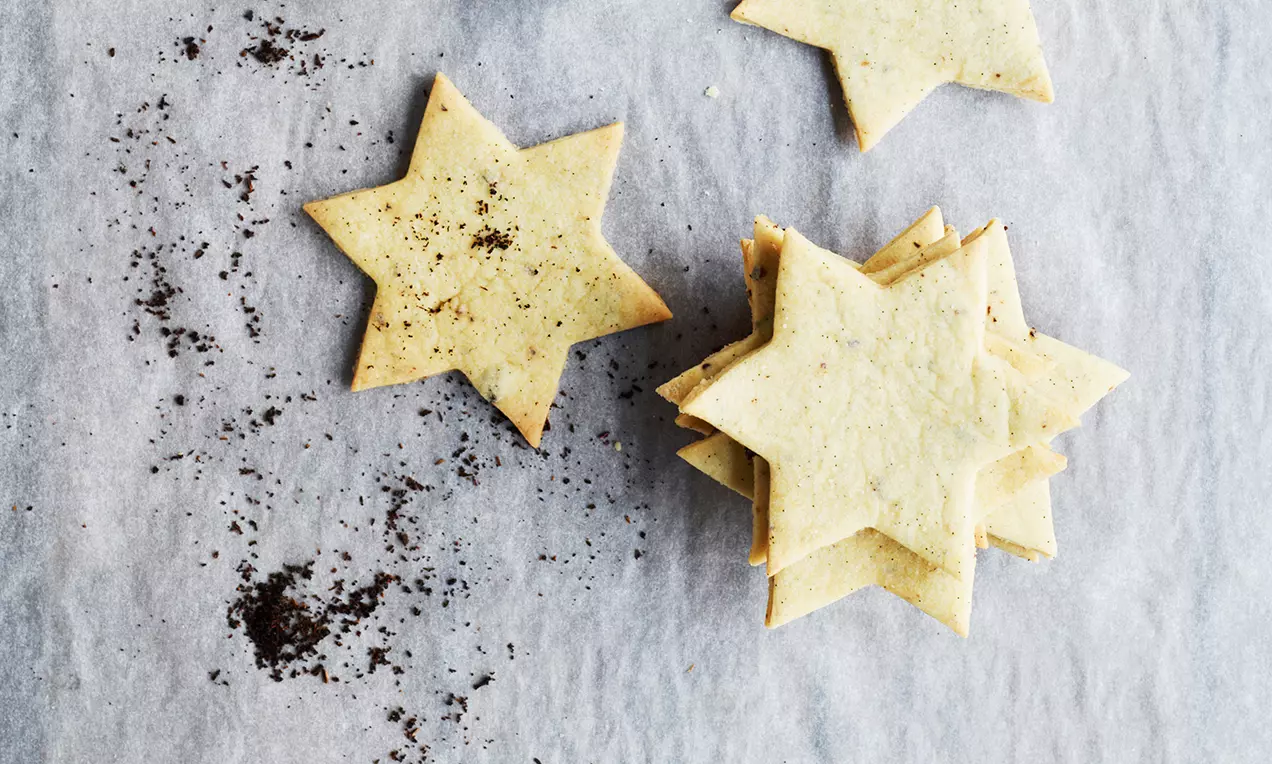 Smørgule stjernekaker med sprø kanter og små svarte vaniljefrø ligger spredt og stablet på et underlag av grått bakepapir