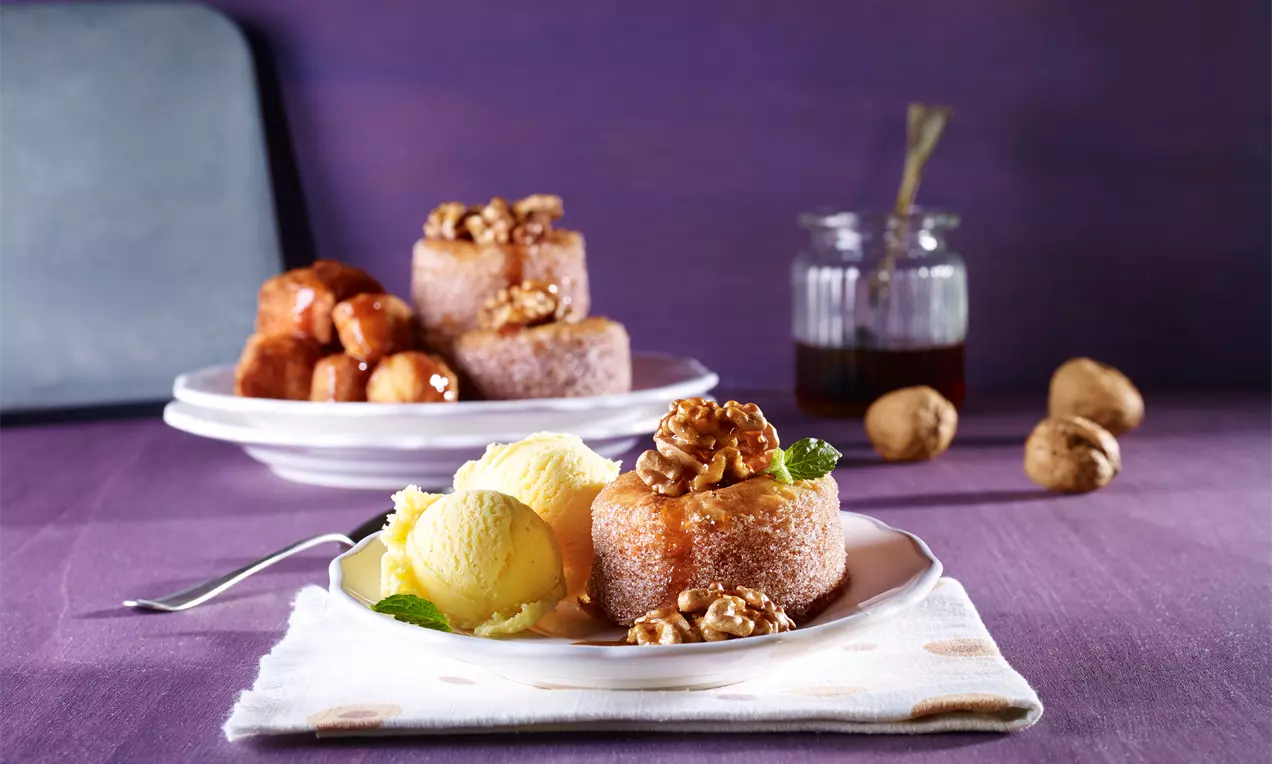 Runde kringlekaker med gyllenbrun overflate toppet med valnøtter og sirup på en hvit tallerken med en kule gul iskrem og mynteblad