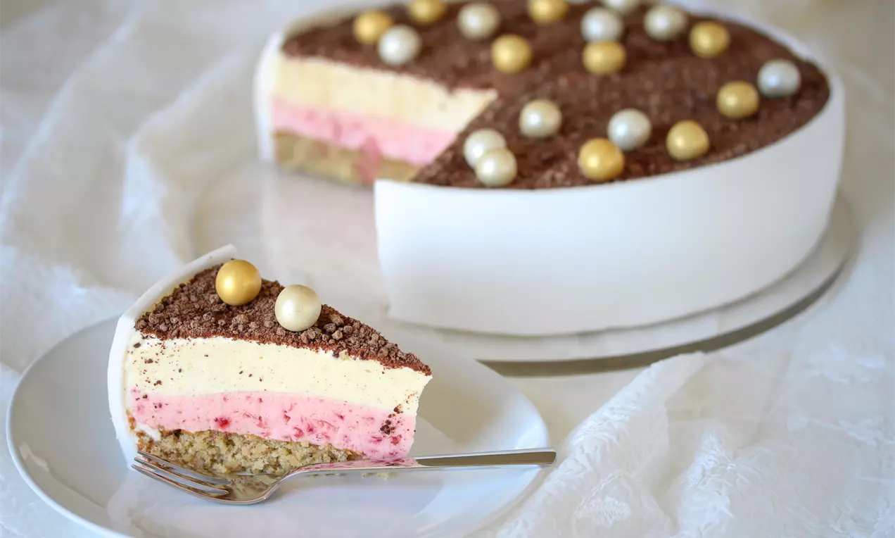 Konfirmasjonskake med lag av lys vaniljefromasj og rosa jordbærfromasj på nøttebunn, toppet med sjokolade og gull- og perlefargede kuler