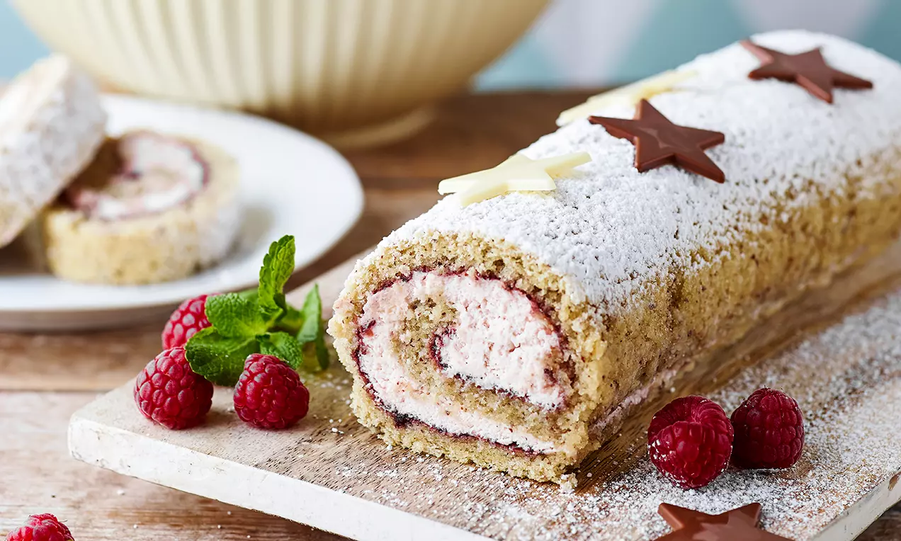 Nøtteroulade med lys brun og sprø overflate, fylt med rosa hindbærskum, drysset med melis, toppet med sjokoladestjerner på et lyst brett
